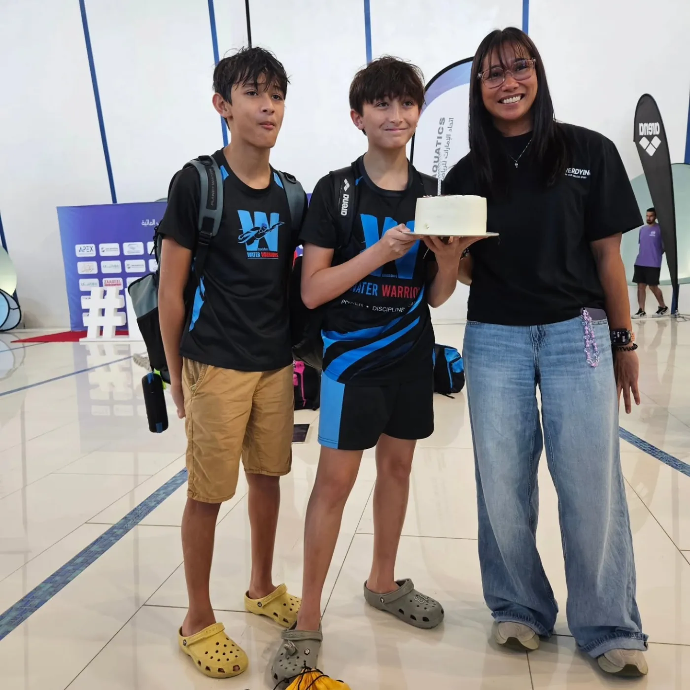 Two teammates and a supporter sharing a cake at a swimming event